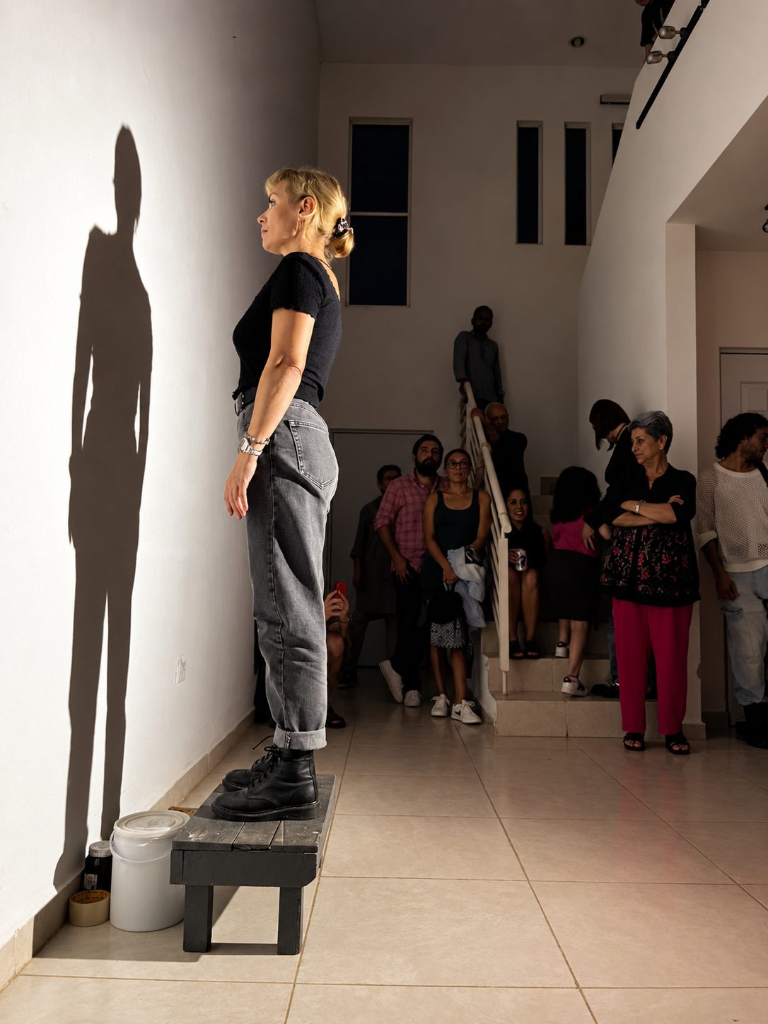 Performance en Ocupa Lorca: una mujer de pie sobre un banco proyecta su sombra en el muro de la galería